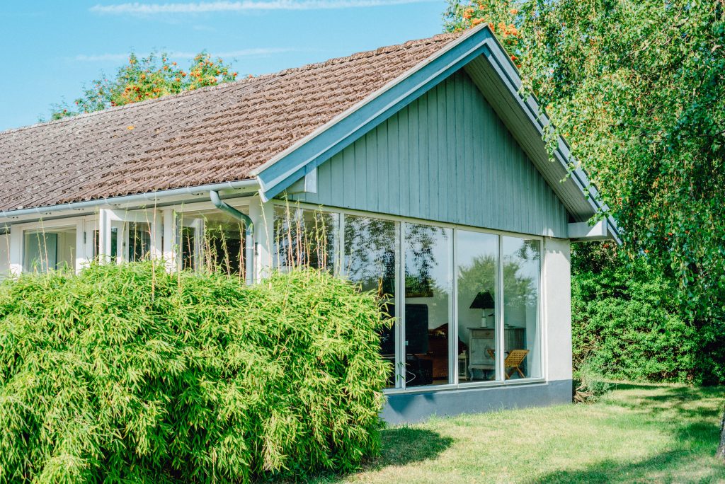 Bright and airy modern cabin with large glass panels surrounded by lush greenery.